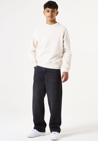 Sweatshirt in lichtbeige, ronde hals, zachte stof; gecombineerd met donkere denim jeans, losse pasvorm, rechte pijpen; witte sneakers maken de outfit compleet.