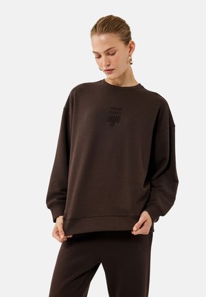 Sudadera marrón oscuro de tejido suave, con cuello redondo de canalé, hombros caídos y texto bordado que dice "DE 1980 nyc."