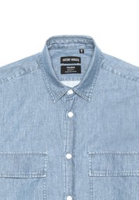 Camicia in denim lavato di colore azzurro chiaro, con colletto a bottone, patta frontale e due tasche sul petto. Presenta un design a vestibilità regolare.
