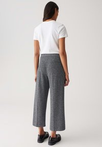Pantaloni larghi grigi heather realizzati in tessuto texturizzato, con vita alta e tasche laterali, abbinati a una maglietta bianca a maniche corte.