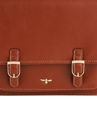 Smeđa kožna torba s preklopom i bijelim šavovima, dva zlatna kopčanja i mali zlatni grb pčele centriran ispod preklopa.