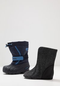 Botte d'hiver bleu marine avec semelle en caoutchouc noire et bride ajustable, associée à une doublure amovible en feutre gris foncé.