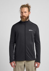 Schwarz gemusterte Fleecejacke mit hohem Kragen und durchgehendem Reißverschluss, ausgestattet mit seitlichen Taschen, weichem Material und Logo auf der linken Brust.