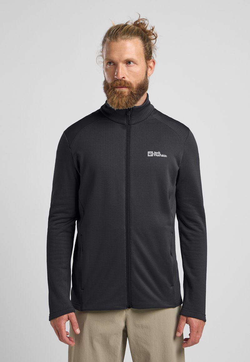 Schwarz gemusterte Fleecejacke mit hohem Kragen und durchgehendem Reißverschluss, ausgestattet mit seitlichen Taschen, weichem Material und Logo auf der linken Brust.