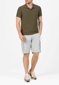Olive green striped polo shirt with three buttons. Light gray cargo shorts with pockets. Casual gray and orange sneakers.