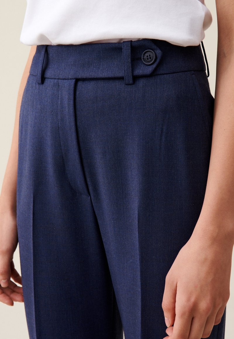 Marineblaue maßgeschneiderte Hose mit flacher Vorderseite, Seitentaschen und einem einzigen Knopfverschluss am Bund. Glattes Textil.