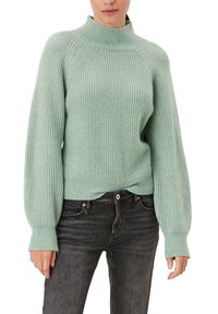 Maglione a maglia verde chiaro con colletto alto, texture a coste e maniche a palloncino, abbinato a jeans di denim scuro.