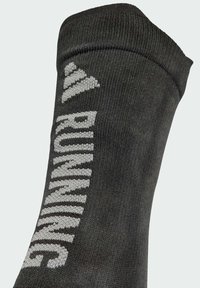 Schwarze Laufsocke mit geripptem Muster, bestickt mit dem Wort „RUNNING“ in grauer Strickoptik. Knöchellang mit enganliegendem Bündchen.