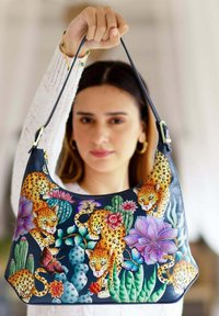 Leren schoudertas met kleurrijke luipaard- en bloemmotieven op een donkere achtergrond; voorzien van een riem met een goudkleurig hardwareaccent.