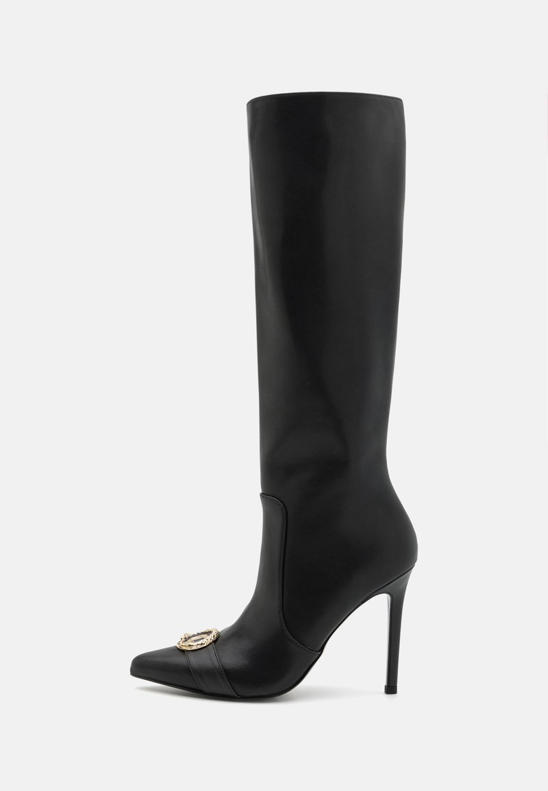 Crne čizme do koljena od kože sa štiklom i šiljastim prstom te zlatnom ukrasnom kopčom sprijeda na bijeloj pozadini.