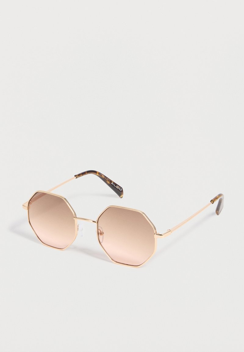 Lunettes de soleil de forme octogonale avec des montures en métal doré fin et des verres à dégradé marron, présentées sur un fond blanc.