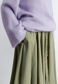 Lavender fuzzy sweater with a relaxed fit paired with a high-waisted, pleated, olive green skirt featuring side pockets and zippers.