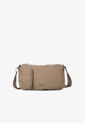 Beige schoudertas met ritssluiting en kwastje, gedragen over de schouder, gecombineerd met een lichtblauwe trui en spijkerbroek.