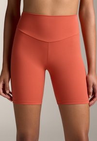 Rövidnadrág magas derékkal, testhezálló fazonban, korall színű, rugalmas anyagból, sima felülettel és minimális varrásokkal a kényelem érdekében.