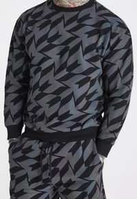 Sudadera de estampado en negro y gris con cuello redondo, puños acanalados y un corte holgado, con un diseño abstracto de formas angulares.