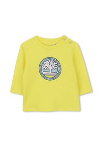 Geel overhemd met lange mouwen, voorzien van een rond, blauw Timberland-logo in het midden. Zacht katoenmateriaal met twee drukknoopsluitingen op de schouder.