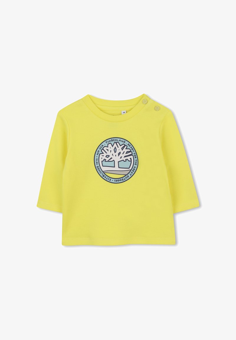 Geel overhemd met lange mouwen, voorzien van een rond, blauw Timberland-logo in het midden. Zacht katoenmateriaal met twee drukknoopsluitingen op de schouder.