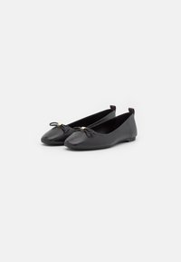 Zwarte leren ballet flats met ronde neuzen, een kleine strikaccent en een goudkleurig detail aan de voorkant. Platte zool met een minimale hak.