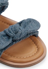 Sandal in tessuto denim blu con design annodato, texture morbida e suola sintetica marrone. Presenta cuciture lungo il bordo.