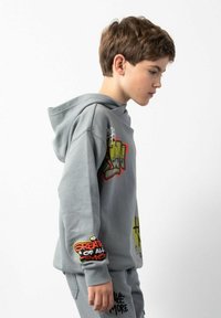 Szara bluza z kapturem z kolorowymi grafikami i tekstem na przodzie i rękawie; miękka tekstura, luźny krój, regulowany kaptur i ściągacze przy mankietach.