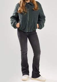 Green, fluffy, zip-up jacket with a high collar and side pockets, paired with black flared jeans and white sneakers.