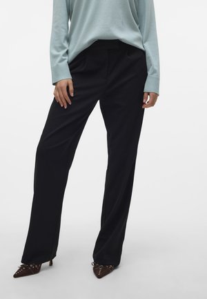 Black wide-leg trousers with a smooth texture, high waist, and crisp pleats, paired with a light blue long-sleeve shirt and brown heeled shoes.