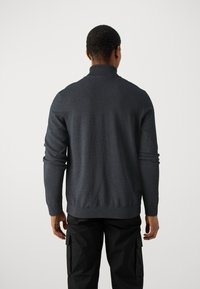 Pull en maille gris foncé à col montant, ourlet et poignets côtelés, doté d'une texture lisse et d'une coupe ajustée. Porté avec un pantalon cargo noir.