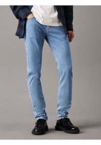 Světle modré džíny z denimu s úzkým střihem, vybavené klasickým designem s pěti kapsami, nošené s černými šněrovacími botami a kostkovanou košilí.