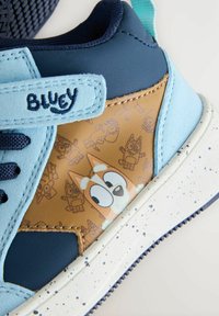 Zapatillas para niños con un diseño azul y marrón claro que presenta un patrón de personajes. Fabricadas con materiales sintéticos y con una suela blanca moteada.