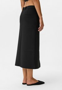 Schwarze Culottes aus glattem Stoff, mit weitem Bein, Gürtelschlaufen und zwei dezenten Gesäßtaschen. Schlichtes Design ohne erkennbare Muster.