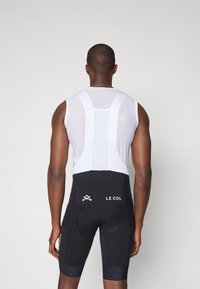 Tenue de cyclisme avec un haut sans manches en mesh blanc et un short rembourré noir. Comprend des détails de logo et un design fuselé et ajusté.