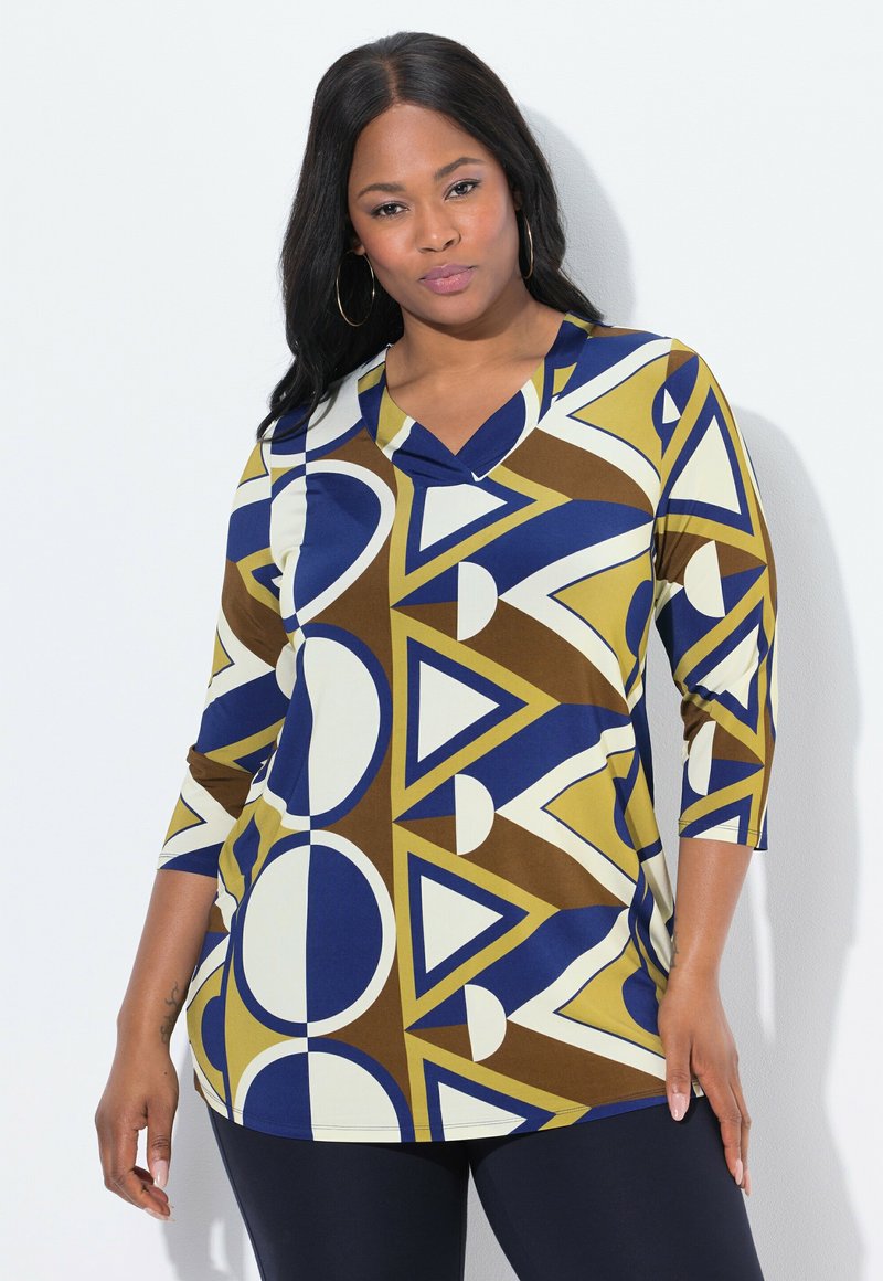 Bunt gemusterte Bluse aus dehnbarem Material mit geometrischen Mustern aus Kreisen und Dreiecken in Blau, Braun, Gelb und Creme. V-Ausschnitt-Design.
