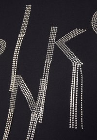 Tissu noir comportant des lettres en rhinestones argentés dans un design moderne. Les accents créent un contraste texturé et brillant avec l'arrière-plan.
