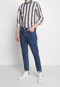 Camicia a righe bianca e blu navy, abbinata a jeans blu scuro in denim e sneaker bianche. I jeans hanno una vestibilità slim e risvolti.