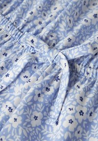 Tissu bleu clair avec un motif floral en blanc et bleu marine, présentant une taille élastique et un détail nœud en tissu.