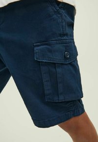 Pantaloni cargo blu navy in cotone, con una tasca laterale con chiusura a bottone e dettagli cuciti. Texture liscia e vestibilità casual.