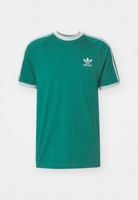 Grön bomull t-shirt med korta raglanärmar, grå krage och kant, samt vitt Adidas-logga på vänster bröst. Slät textur, avslappnad passform.
