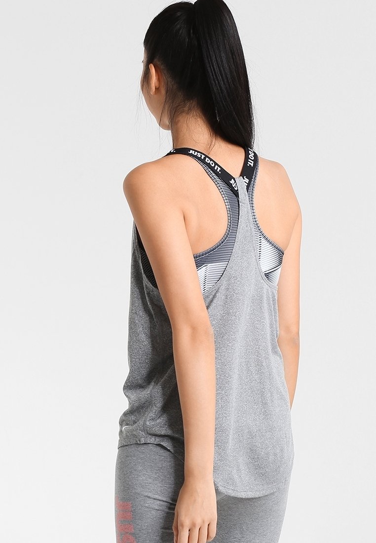 Femme avec queue de cheval noire portant un débardeur gris et un soutien-gorge de sport avec les bretelles "Just Do It", de dos sur fond uni.