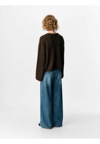 Brun, stickad tröja med avslappnad passform och sänkta axlar, ihop med vida blå denimjeans. Mjuk textur och avslappnad silhuett.