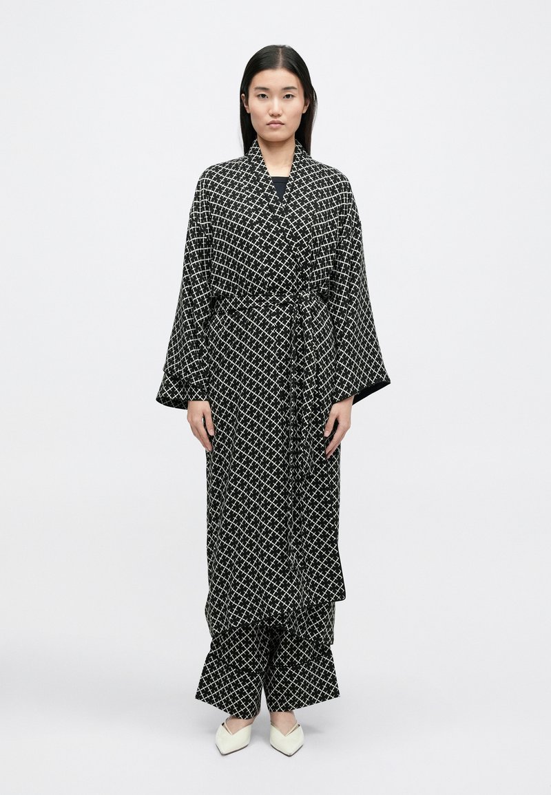 Schwarz-weiße, gemusterte Kimono-Robe im Stil mit weiten Ärmeln, tailliertem Gürtel und passenden Hosen; das Material wirkt glatt mit einer feinen Textur.