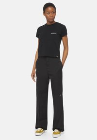 Zwarte cropped t-shirt met een klein wit logo, gecombineerd met hoge zwarte wijde broek met zijzakken en een subtiele merketiket.