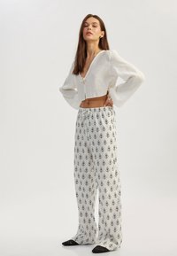 Vit kort blus med V-ringning och puffärmar, matchad med högmidjade, löst sittande byxor med svart blommönster.