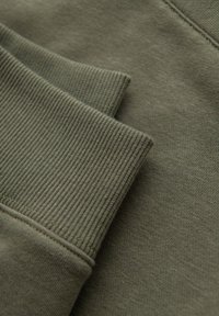 Nærbillede af olivengrønne ribstrikkede manchetter på blødt bomuldsstof, der viser detaljeret tekstur og syning.