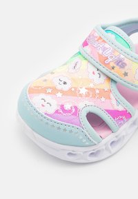 Kolorowe sandały dla dzieci z wzorami chmur i gwiazd, posiadające świecącą podeszwę oraz regulowany pasek. Materiały obejmują miękki syntetyczny wierzch.