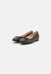Ballerine in pelle nera con punta tondeggiante, bordi scallop e un dettaglio a fiocco decorativo sulla parte superiore. Tacco basso e piatto.