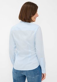 Light blue long-sleeve shirt made of smooth fabric, featuring a classic collar, buttoned cuffs, and a tailored fit with a curved hem.