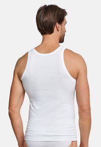 Top in cotone bianco a coste, morbido al tatto, con scollatura rotonda e spalline larghe, visto da dietro.