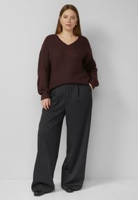 Dzianinowy bordowy sweter z dekoltem w serek o prążkowanej fakturze, zestawiony ze spodniami o szerokich nogawkach w czarną prążkę, z przodu z zakładkami i bocznymi kieszeniami.