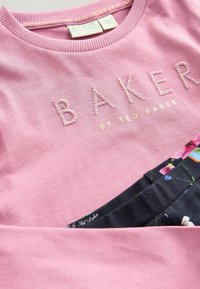 Rosa bomulds-sweatshirt med ribbet halsudskæring, der har "BAKER" broderet i bogstaver og en blomster nederste panel med mørkere baggrund.