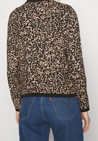 Striktrøje med et abstrakt mønster i sort og tan, med rund hals og ribbede manchetter. Kombineret med blå denimjeans.